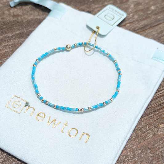 Hope Unwritten Bracelet - Turq It Girl by eNewton. Made with 2mm turquoise seed beads and 2mm 14k gold-filled beads. Measures standard (6.25"). Hand beaded on high performance elastic for a slight stretch to easily roll on and off your wrist Worry-free wear‚ sleep, shower and sweat in it. Stacks well with all bracelets. Shop at The Painted Cottage in Edgewater, MD.
