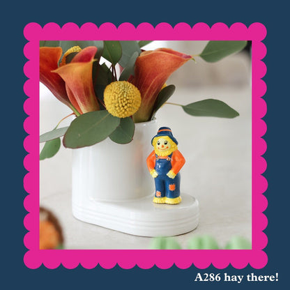 A286 Hay There! Scarecrow mini in yellow, blue and orange. by Nora Fleming. Shop at The Painted Cottage in Edgewater, MD.