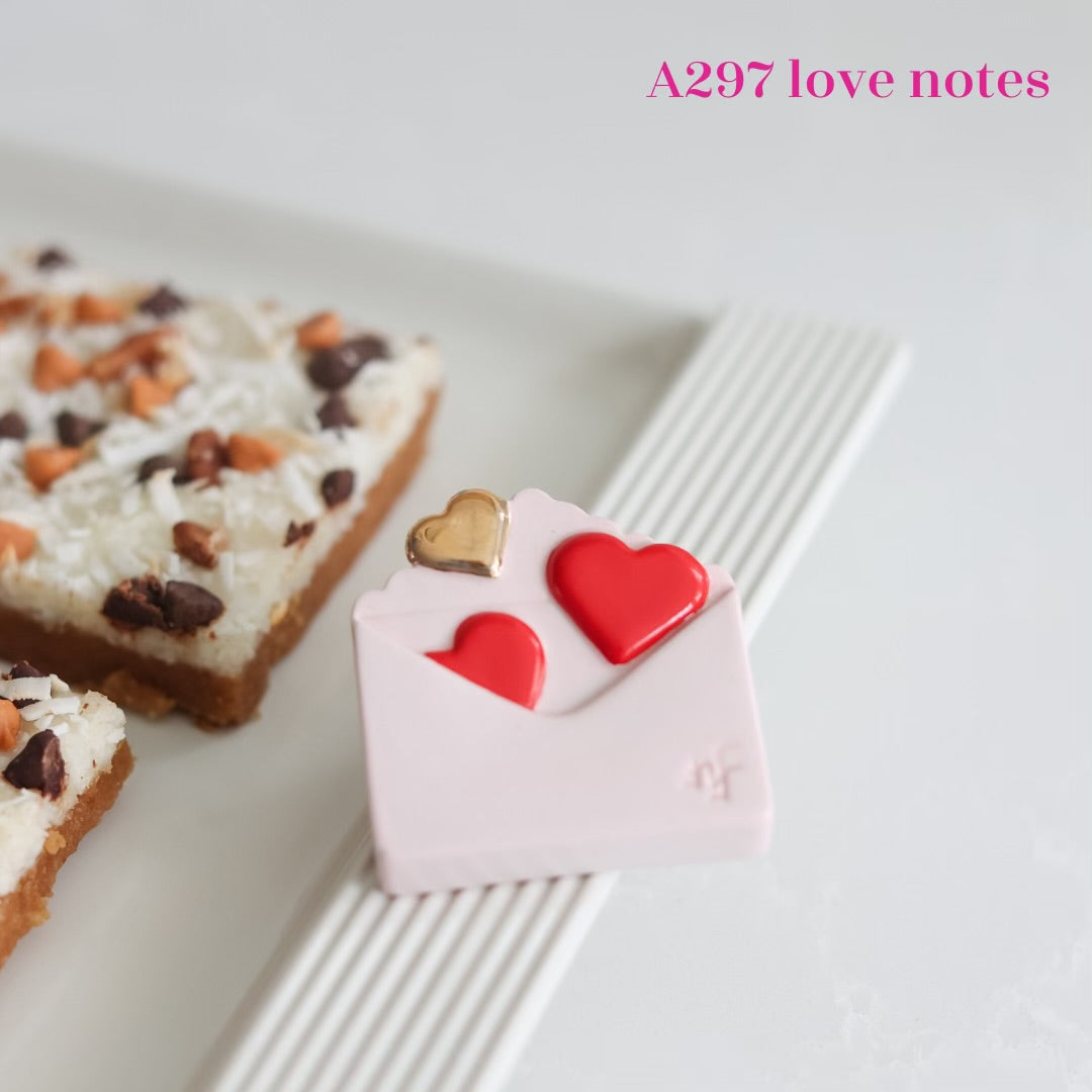 A297 Love Notes Mini by Nora Fleming features white envelope with red and gold hearts. Shop at The Painted Cottage in Edgewater MD.